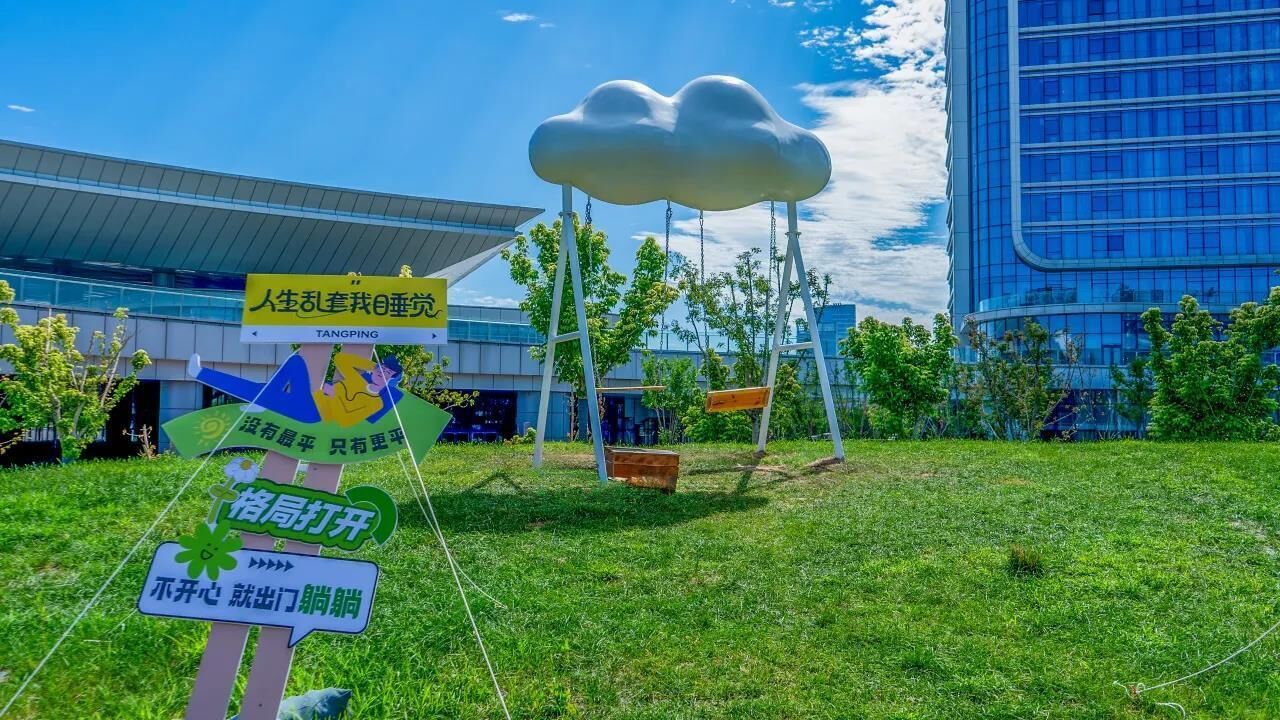 A grassy area with a large white cloud sculpture, a building with a modern design, and a sign with Chinese characters.