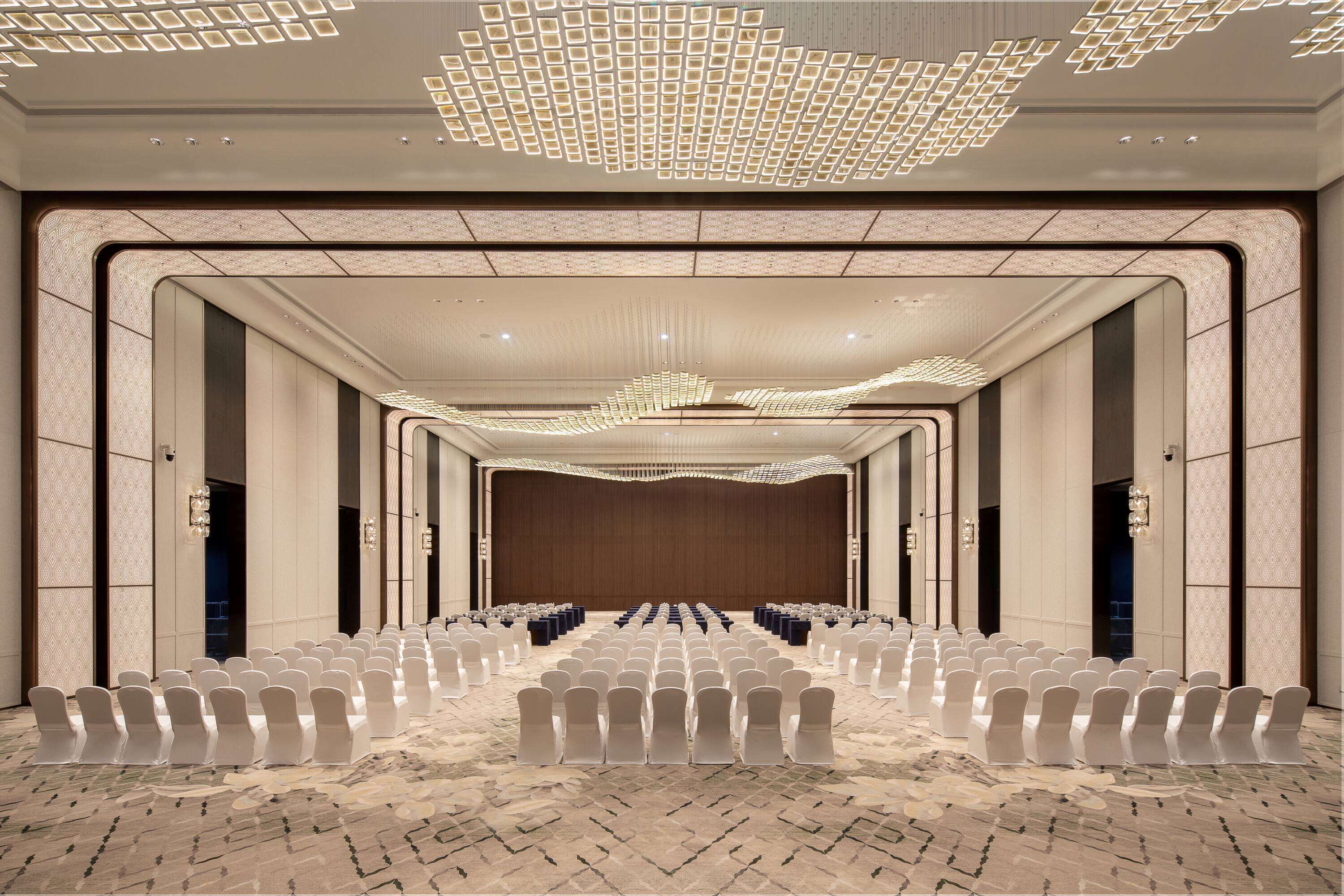 A conference room with rows of chairs, a large screen, and a patterned carpet.