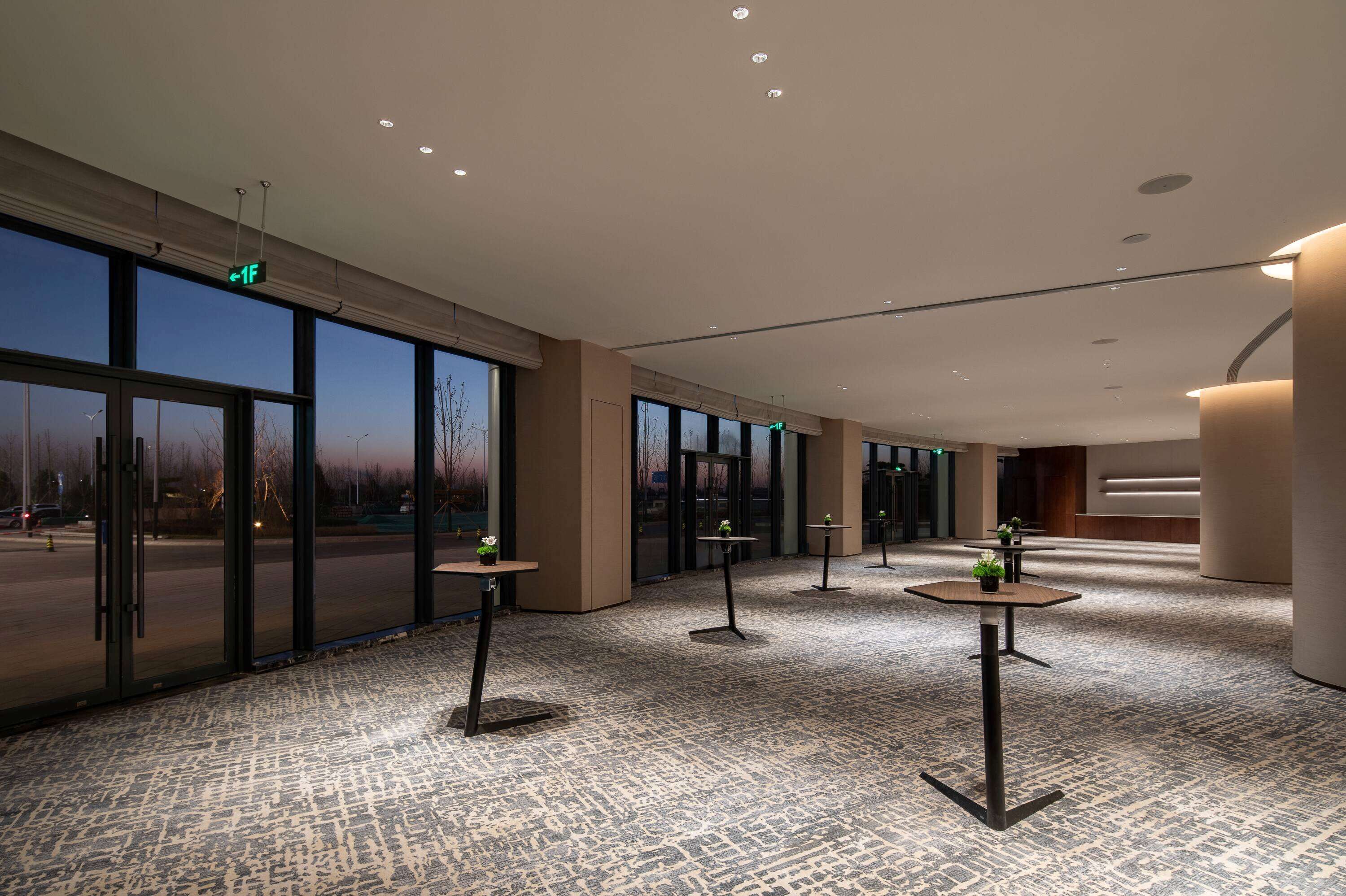 Un hall d’entrée spacieux, doté de grandes fenêtres, de plusieurs tables ornées de plantes et d’un sol recouvert de moquette.