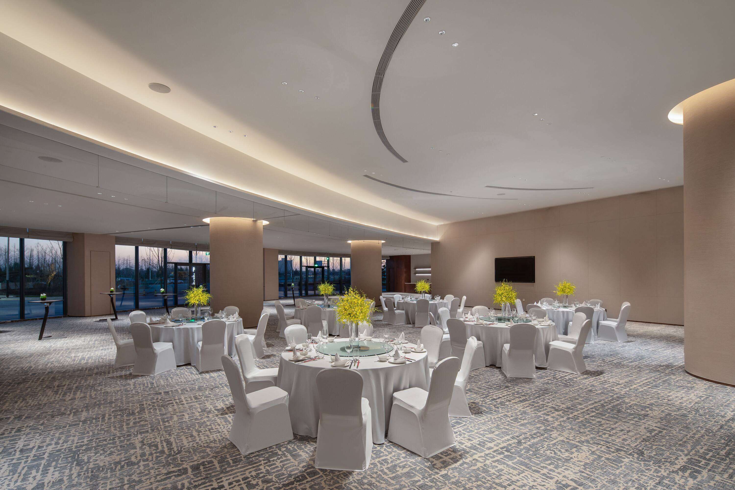 A spacious conference room with round tables, white chairs, and yellow flowers.