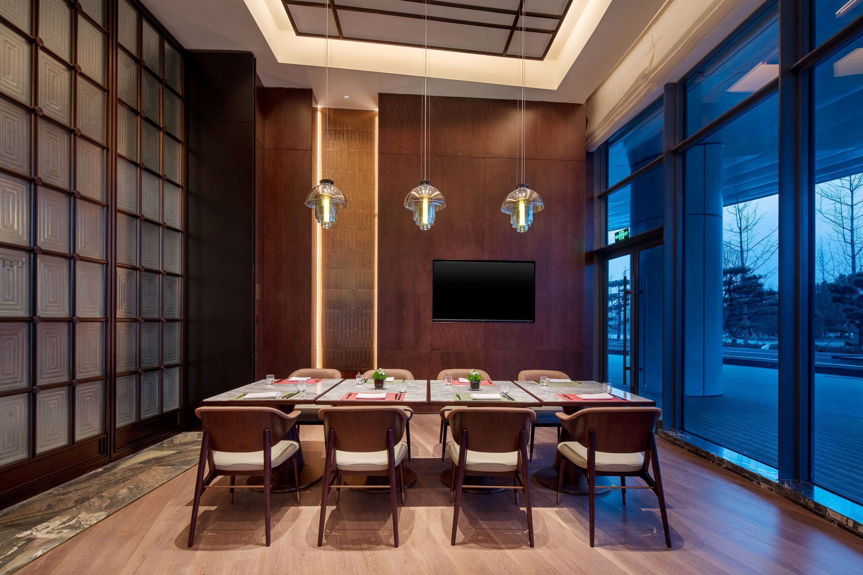 A modern conference room with a long table, six chairs, and three pendant lights.