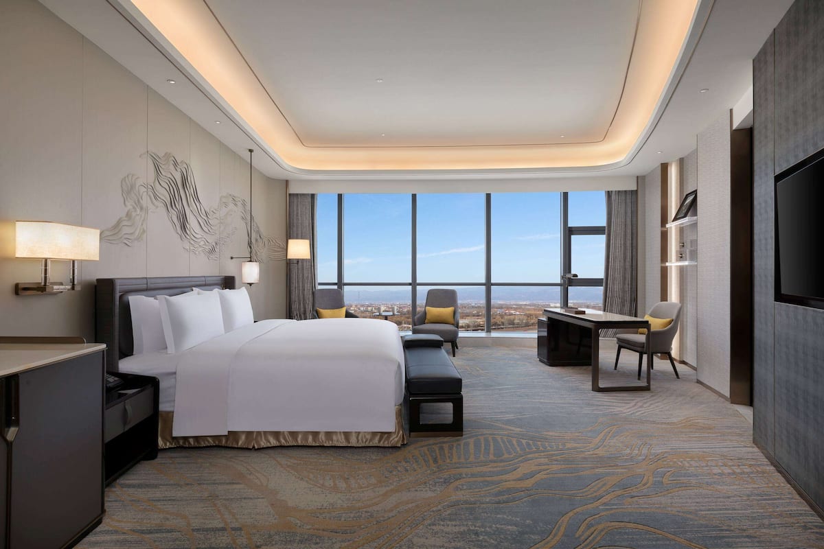 A modern hotel room with a large bed, a desk, and a view of the city.