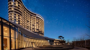 A modern hotel with a curved facade, large windows, and a starry night sky. - Wyndham Grand Shanxi Xiaohe Xincheng (Taiyuan)