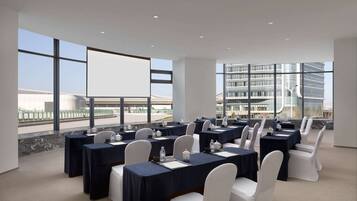 A conference room with tables set for a meeting, large windows offering views of a cityscape, and a modern building in the background.