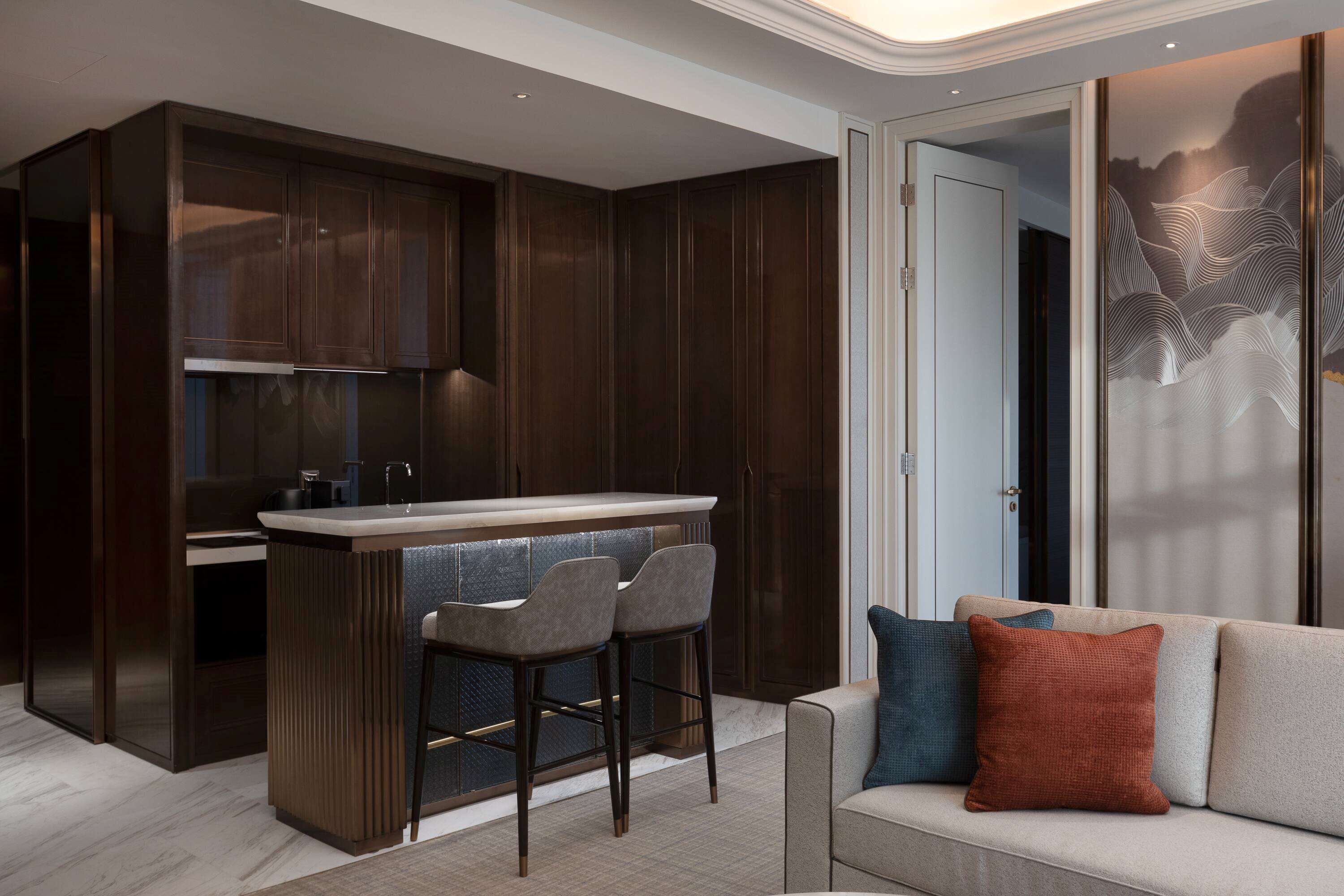 Una cocina moderna con armarios de madera oscura, una isla central con taburetes de bar y encimera de color claro.