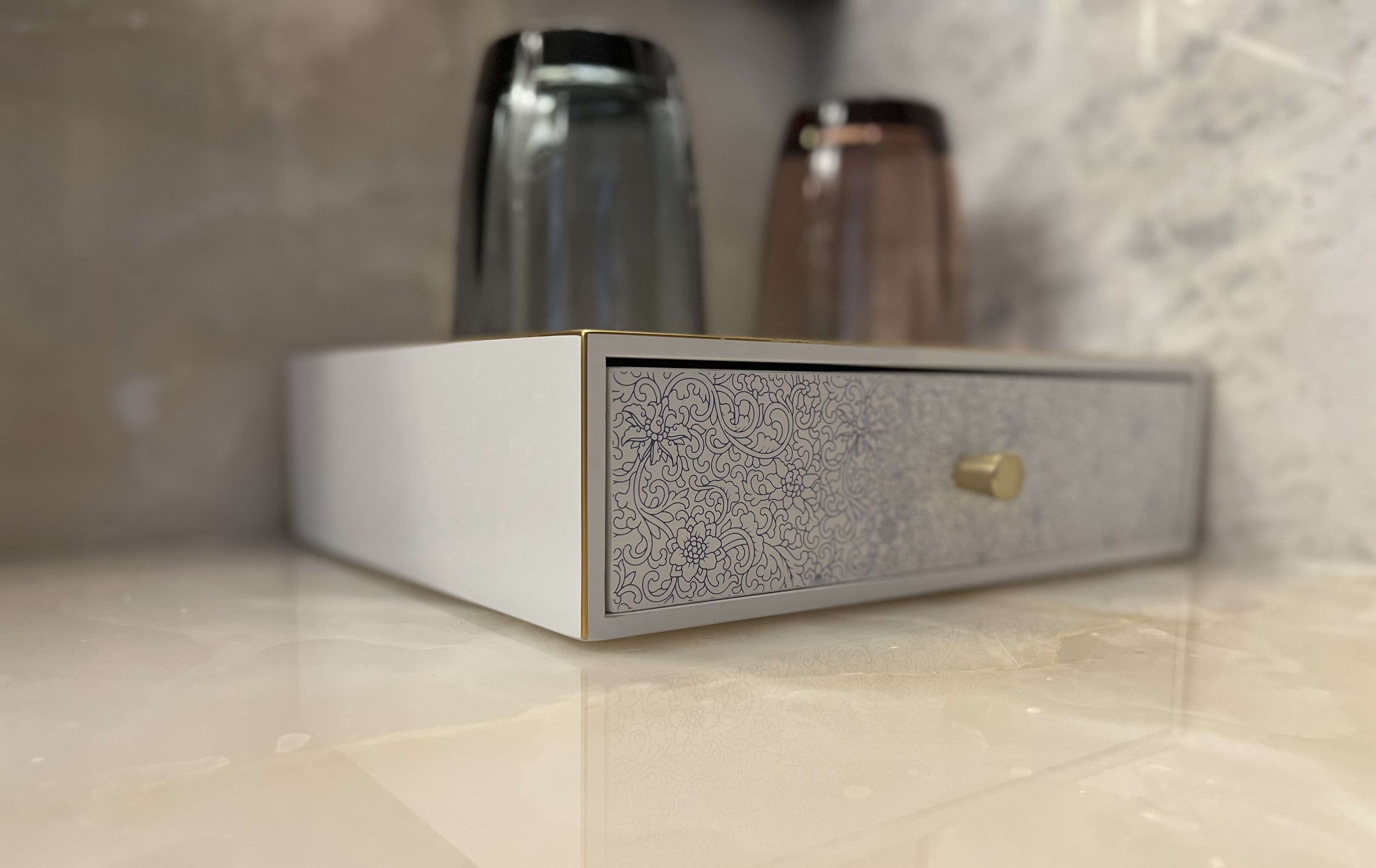 A white, textured box with a brass knob, placed on a marble surface.