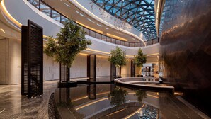 A spacious atrium with a glass ceiling, reflecting the interior and a tree, and a central water feature. - Wyndham Grand Shanxi Xiaohe Xincheng (Taiyuan)