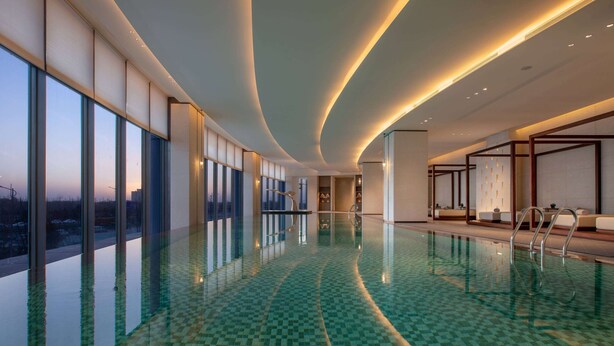 A modern indoor swimming pool with a checkered floor, large windows, and a view of the cityscape. - Wyndham Grand Shanxi Xiaohe Xincheng (Taiyuan)