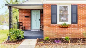 A brick house with a green door, black shutters, and a small porch with a bench. - Single-Level Kingsport Home · Sleeps 6 · Pets OK (Kingsport)