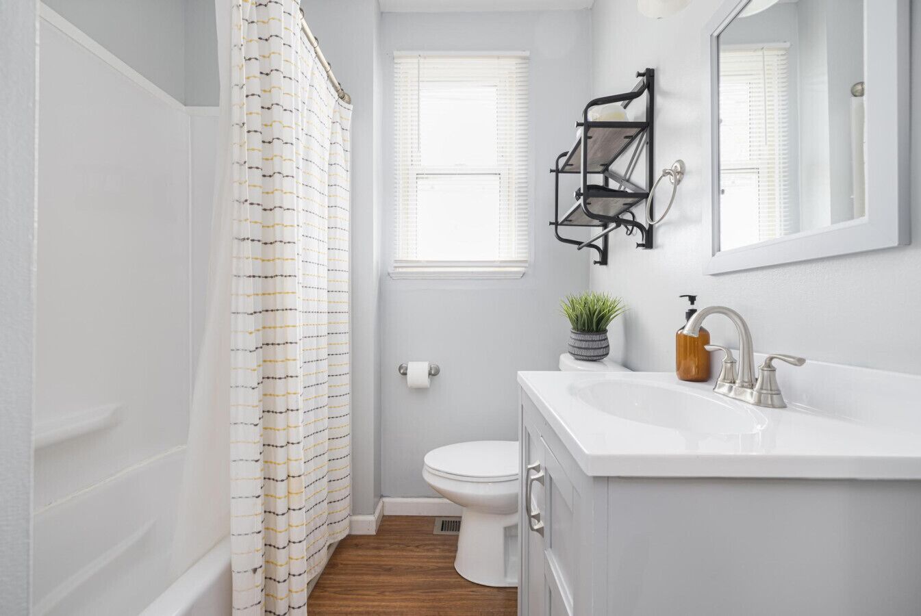 A bathroom with a white toilet, a white sink with a soap dispenser, a small potted plant, a black towel rack, and a shower curtain with a striped pattern.