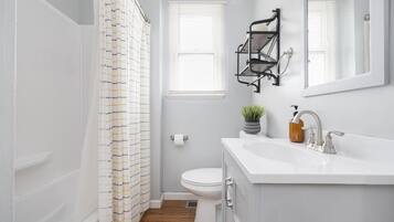 A bathroom with a white toilet, a white sink with a soap dispenser, a small potted plant, a black towel rack, and a shower curtain with a striped pattern.