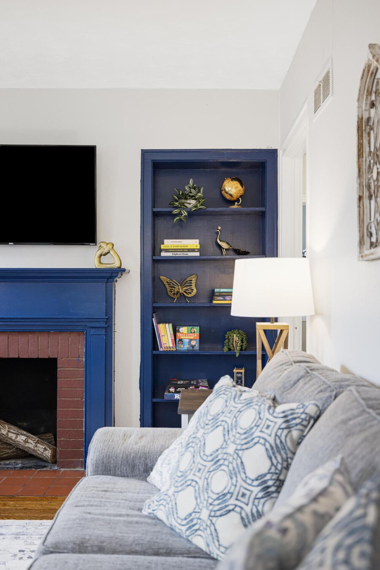 A living room with a blue bookshelf, a fireplace, a flat-screen TV, and a patterned throw pillow on a grey sofa.