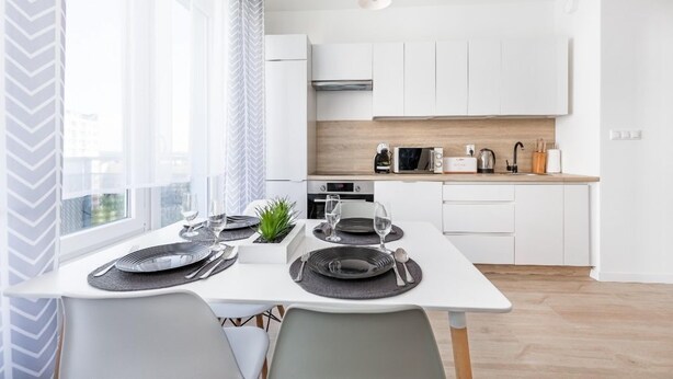 A modern kitchen with white cabinetry, a wooden countertop, and a dining area set for two with a table and chairs.