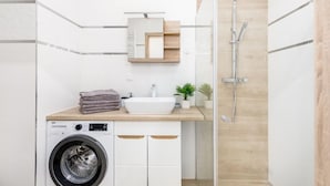 A modern bathroom with a washing machine, a sink, a mirror, and a shower.