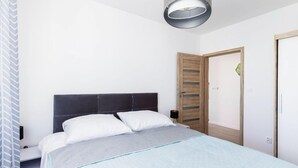 A bedroom with a bed, a nightstand, a wooden wardrobe, and a modern light fixture.