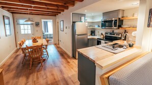 Une cuisine moderne avec des poutres en bois, des appareils électroménagers en acier inoxydable et un coin repas avec des chaises en bois.