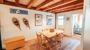 Un coin repas avec une table et des chaises en bois, un banc en bois et des décorations murales, notamment un panneau indiquant « Maine » et un tableau encadré.
