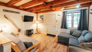 Un salon chaleureux avec des poutres en bois, un canapé, un fauteuil, un téléviseur et une pancarte sur laquelle on peut lire : « SKI THE EAST ».