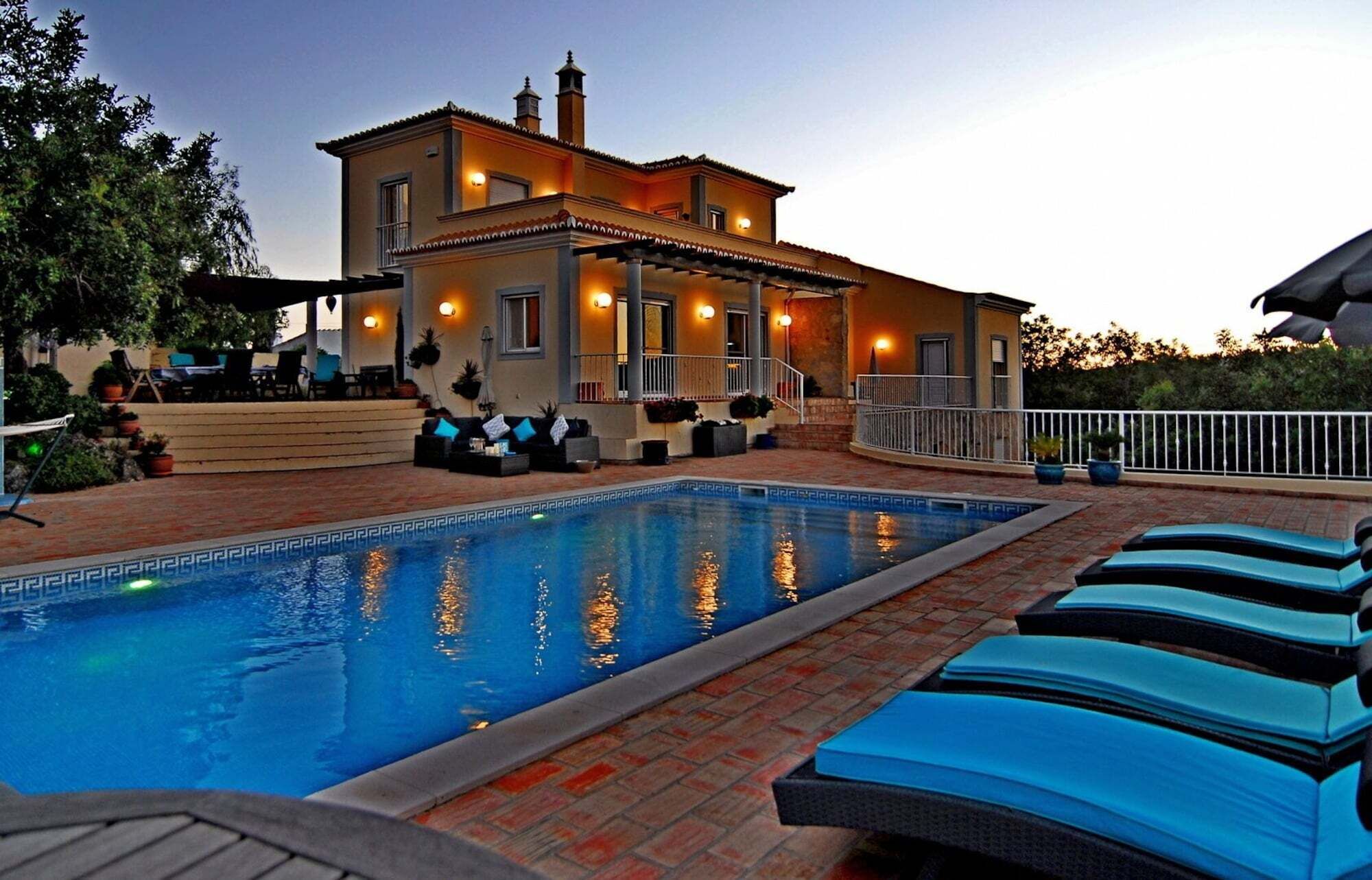 A pool area with lounge chairs, a building with a balcony, and outdoor lighting.