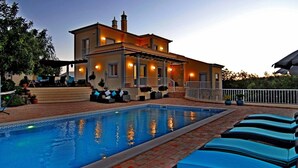 Ein Poolbereich mit Liegestühlen, ein Gebäude mit Balkon und Außenbeleuchtung.