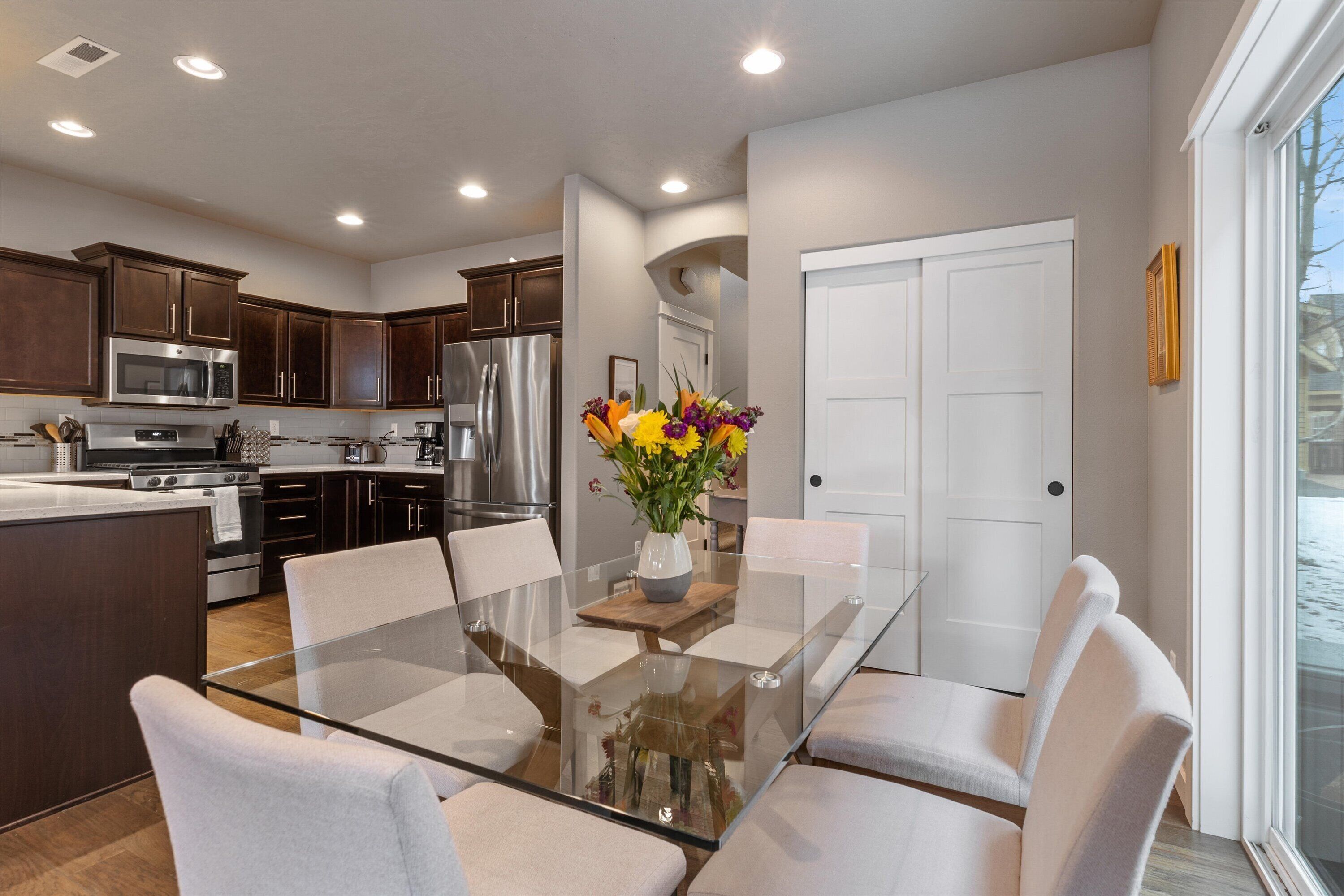 A modern kitchen with dark wood cabinets, stainless steel appliances, and a glass dining table with white chairs.