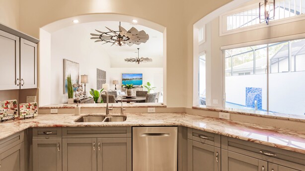 A modern kitchen with a central island, stainless steel appliances, and a large window providing a view of the outdoors. - Ideal Location West of 41 - Minutes to the Beaches! (Naples)