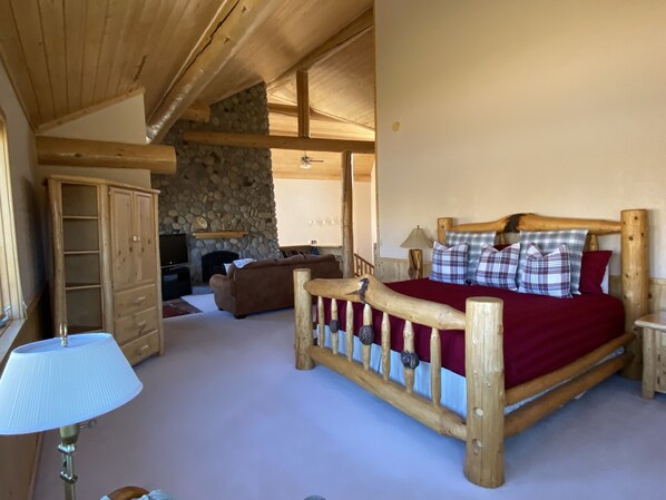 Ein Schlafzimmer mit einem hölzernen Bett, einer Steinwand, einem Holzschrank und einem Fernseher in rustikaler Blockhütten-Atmosphäre.