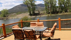 Une terrasse dotée de mobilier d’extérieur, offrant une vue sur une rivière et des montagnes.