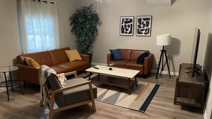 Una sala de estar con dos sofás, una mesa de centro, una lámpara de pie, un mueble para televisor y una planta grande.