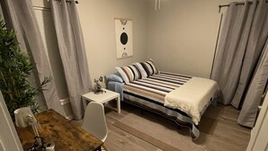 Un dormitorio con cama, escritorio, silla, ventilador de techo y una planta.