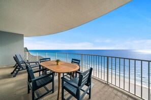 A balcony with a wooden table and chairs, overlooking a beach with a railing.