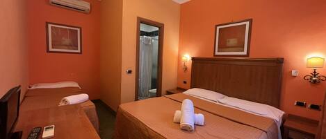 A hotel room with two beds, a desk, a chair, and a bathroom visible through an open door.