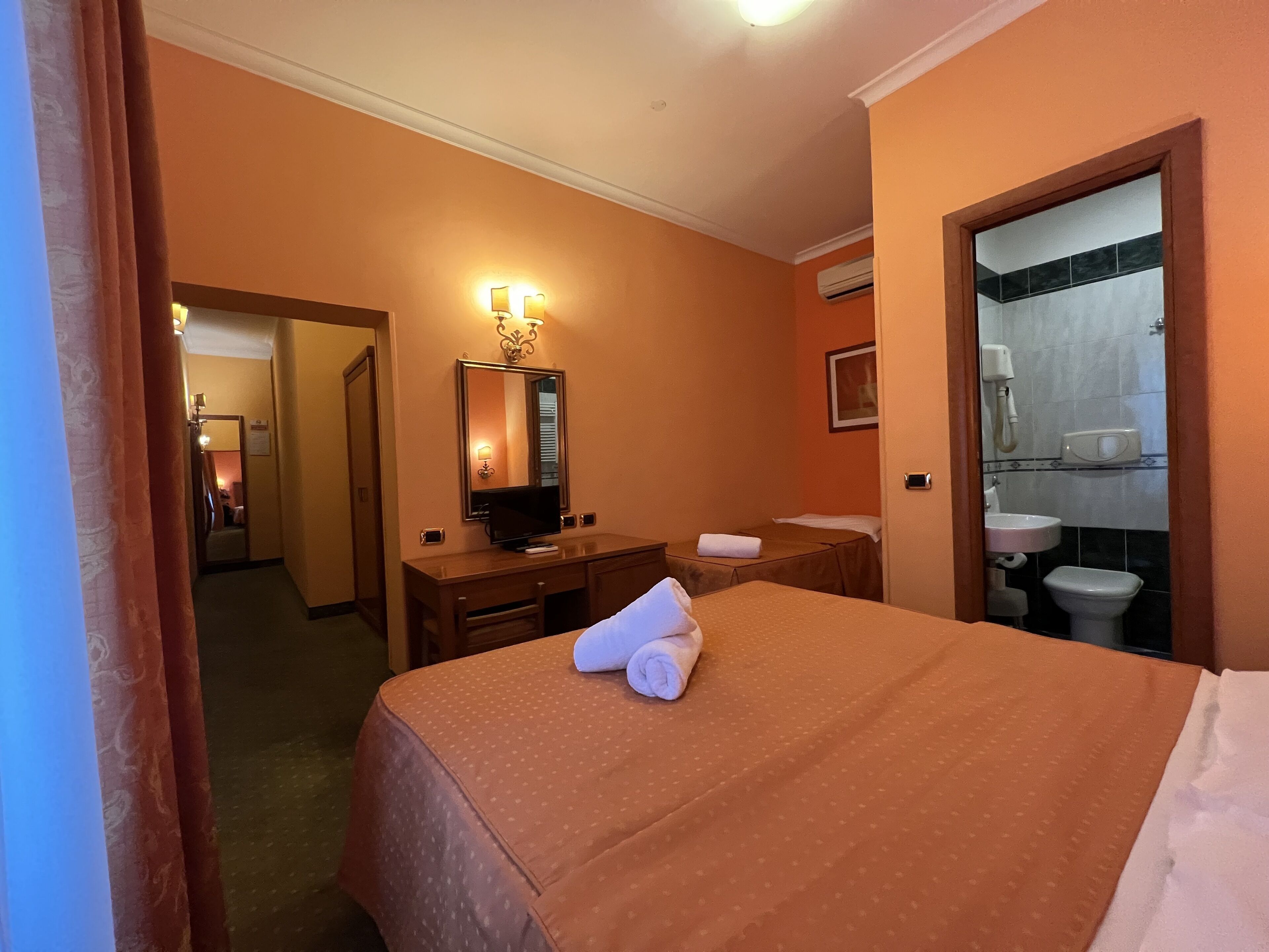 Habitación de hotel con cama, escritorio, espejo y baño con lavabo e inodoro.