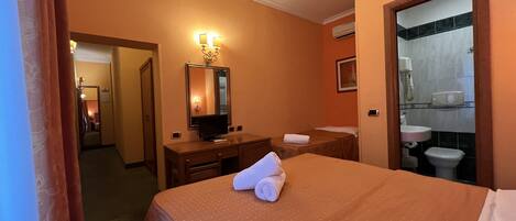 A hotel room with a bed, a desk, a mirror, a bathroom with a sink and toilet.