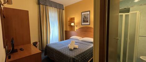 A hotel room with a bed, a desk, a chair, a shower, and a toilet.