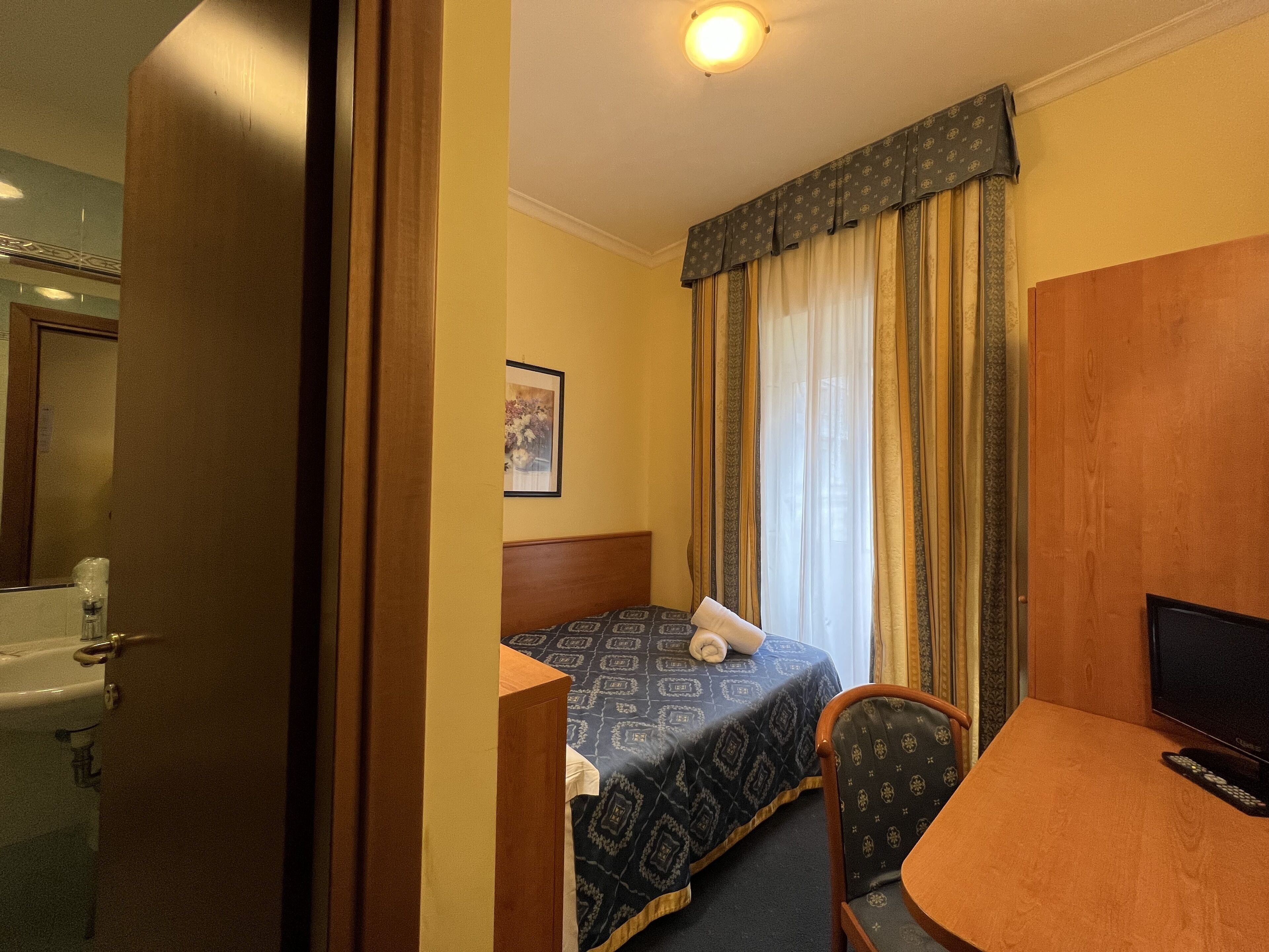 A hotel room with a bed, a desk, a chair, a television, and a bathroom.