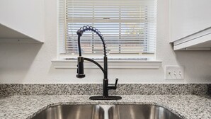 Una cocina con un lavamanos doble de acero inoxidable, encimera de granito y una ventana con persianas.