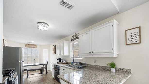Cocina moderna con armarios blancos, encimeras de granito y una isla central. Cuenta con una zona de comedor con mesa y sillas, además de una isla de cocina con taburetes de bar.