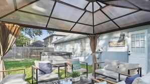 Un patio techado con mobiliario exterior, una mesa de vidrio y un cartel de bienvenida en la pared.