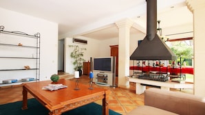 A living room with a wooden table, a sofa, a TV, and a large black chimney. - Cozy Villa w/ Heatable Pool & BBQ (Albufeira)
