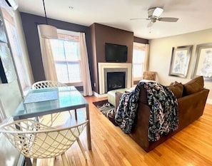 A living room with a fireplace, a television, a dining table with chairs, and a ceiling fan. - Tannersville 1BR on Main Street (Tannersville)