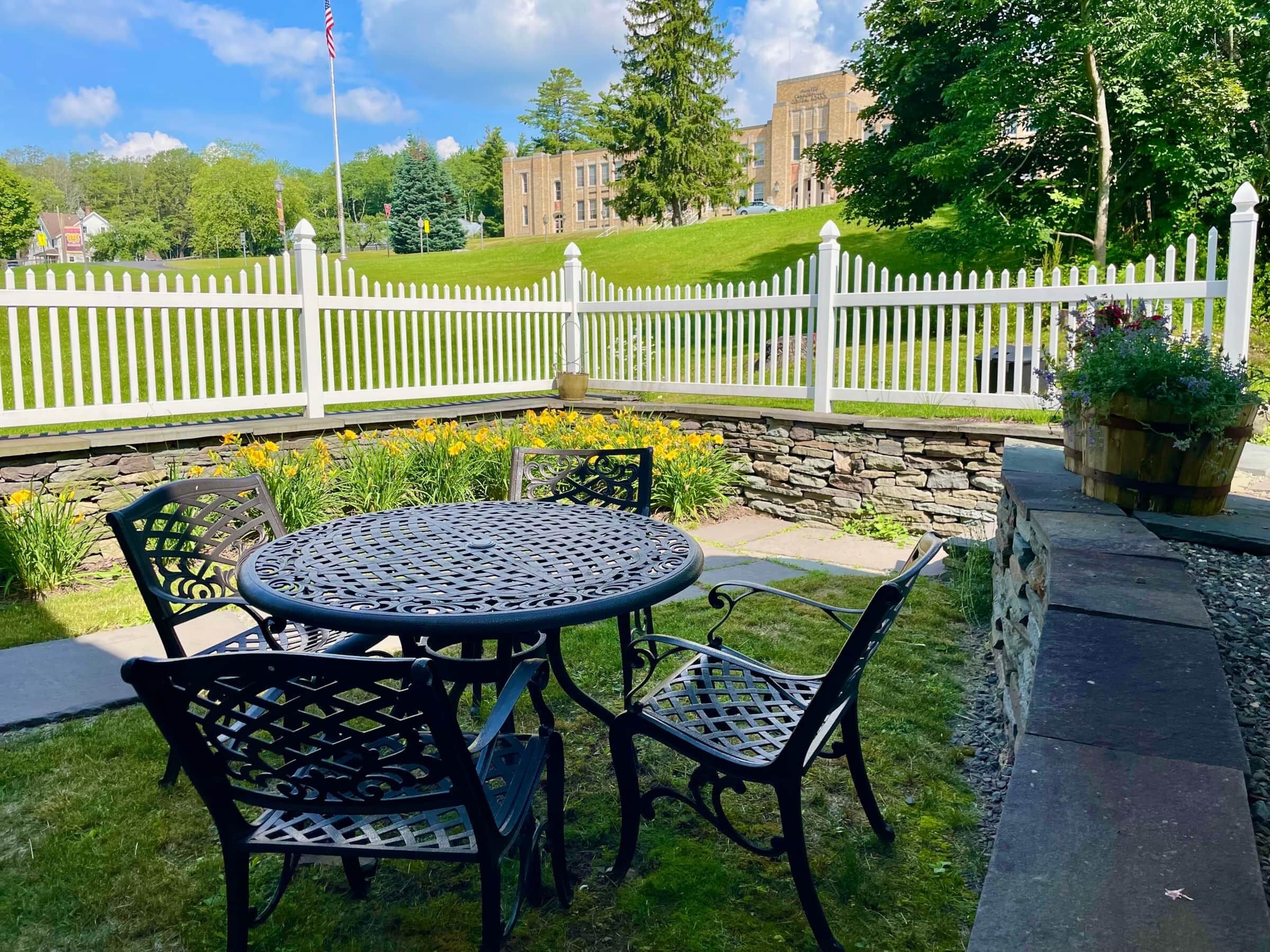 A patio with a round table and four chairs, surrounded by a white picket fence and a stone wall.