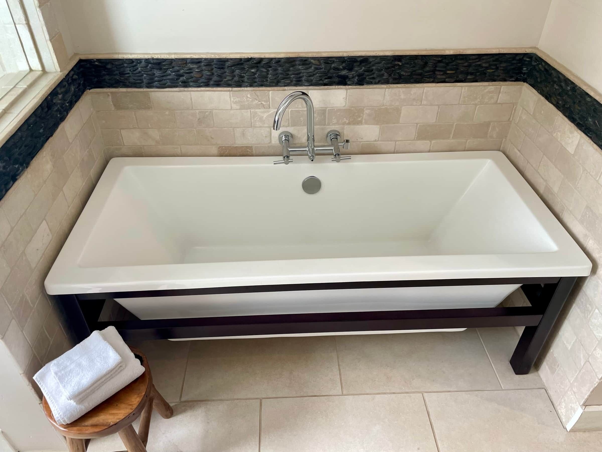 A rectangular bathtub with a single faucet, set in a corner with a dark countertop and beige tiled walls.