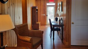 A wooden-paneled room with a wicker chair, a table with a lamp, and a door. - Lake Marion's Big Red House. W/ Dock and Kayaks. Pet Friendly please read policy (Manning)