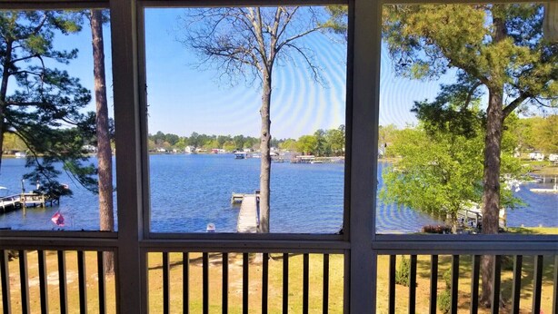 A view from a room with a wooden deck overlooking a lake, docked boats, and a grassy area with trees. - Lake Marion's Big Red House. W/ Dock and Kayaks. Pet Friendly please read policy (Manning)