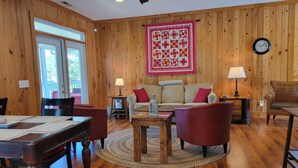 A cozy living room with wooden walls, a round coffee table, a sofa, and a dining table with chairs. - Lake Marion's Big Red House. W/ Dock and Kayaks. Pet Friendly please read policy (Manning)