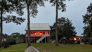 A lakeside cabin with a prominent red exterior, a wooden deck leading to the water, and a small dock. - Lake Marion's Big Red House. W/ Dock and Kayaks. Pet Friendly please read policy (Manning)