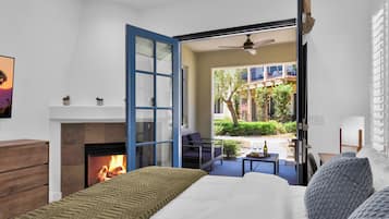 A bedroom with a fireplace, a bed, a view of the outside, and a dining area with a table and chairs.