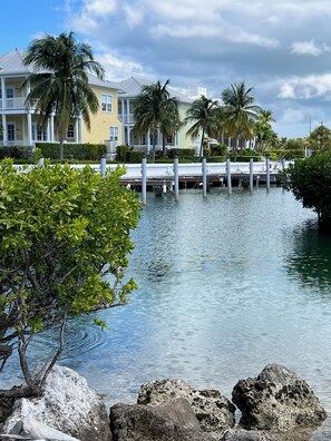 A waterfront property with a dock extending into calm water, surrounded by lush greenery and palm trees. - Beautiful Island Home in Anglers Reef! Ocean front community. Pool & boat slip. (Islamorada)
