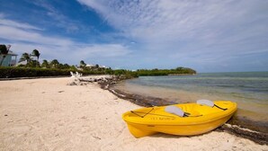 Un kayak jaune sur une plage de sable, avec un ciel dégagé et une île visible au loin.